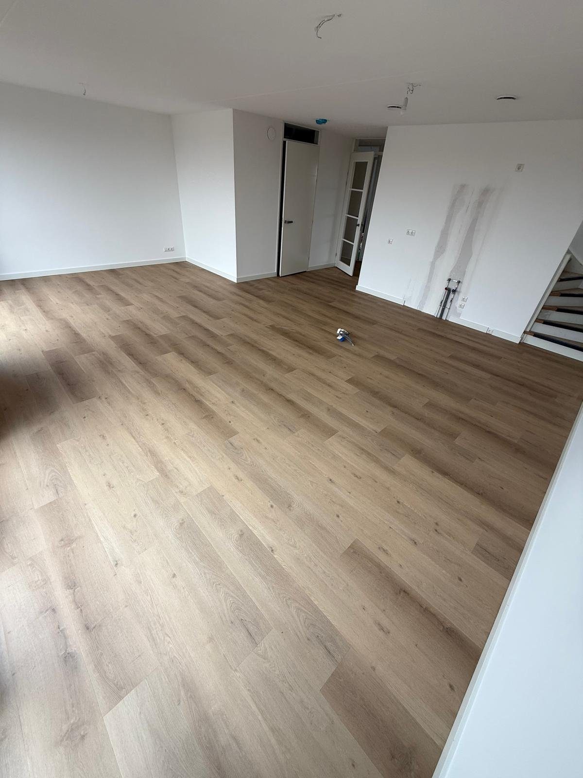 Grote open woonkamer met doorkijk naar trap en meerdere ruimtes, volledig gelegde rechte plankenvloer, gereedschap nog op de vloer.