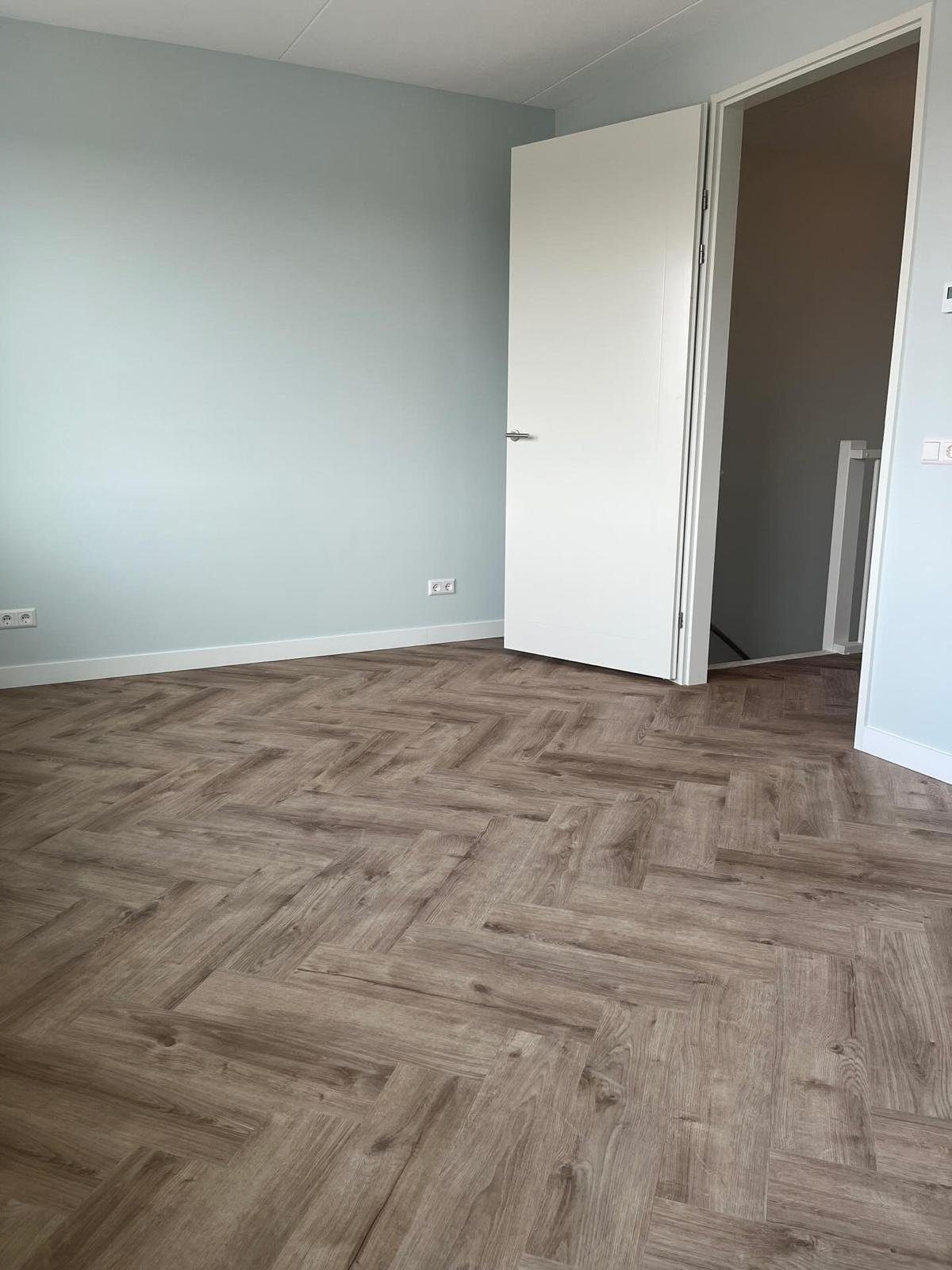 Ruime, lichte woonkamer met openslaande tuindeuren en volledig gelegde visgraat PVC-vloer.