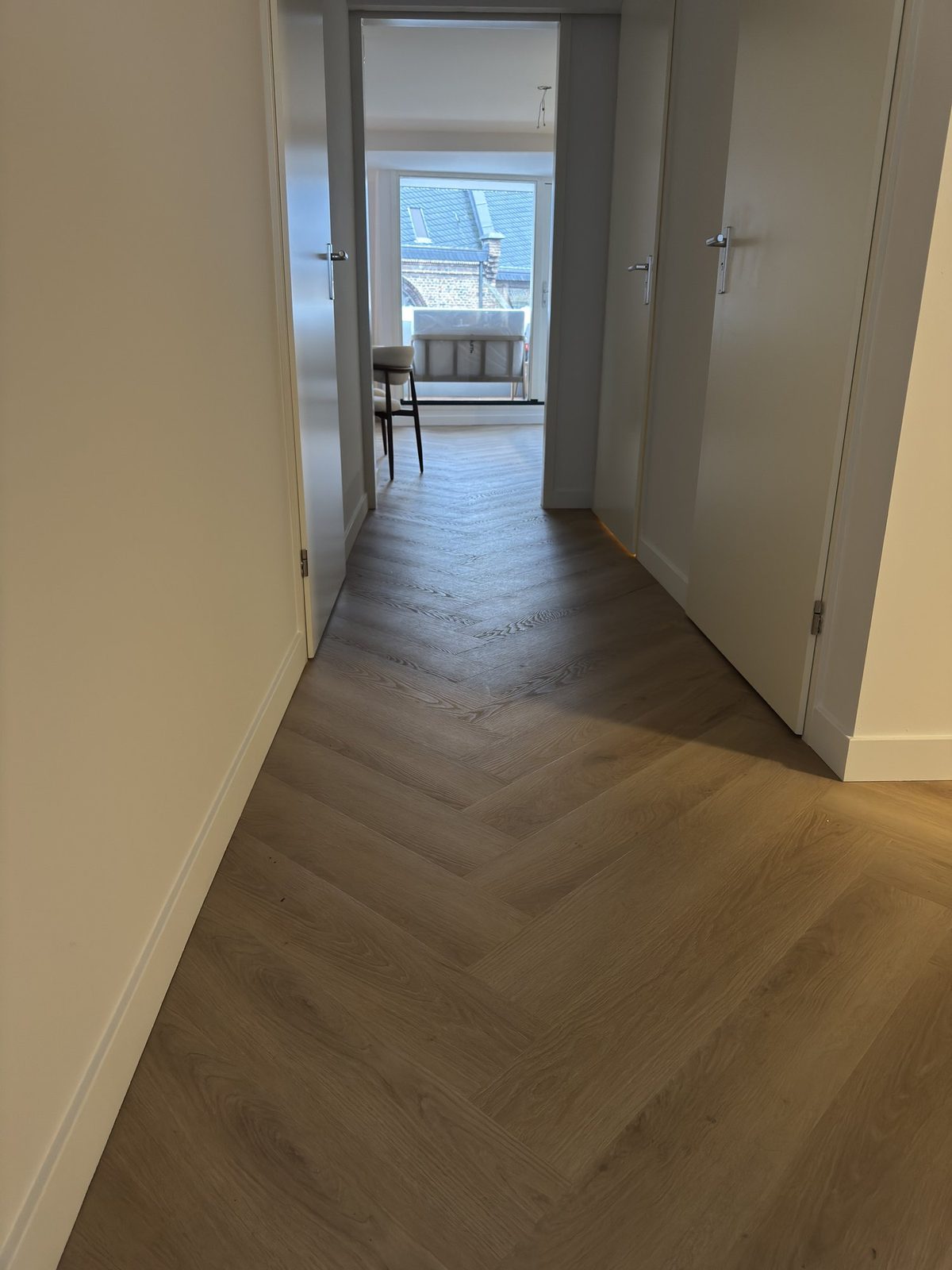 Doorkijk vanuit een gang naar een kamer met een volledig afgewerkte visgraat vloer en zicht op een dakraam.