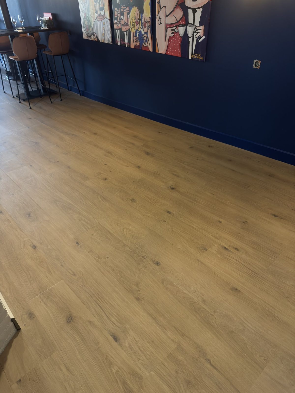 Ruime, overwegend lege houtlook PVC-vloer in een restaurant met kunst aan de blauwe wand.